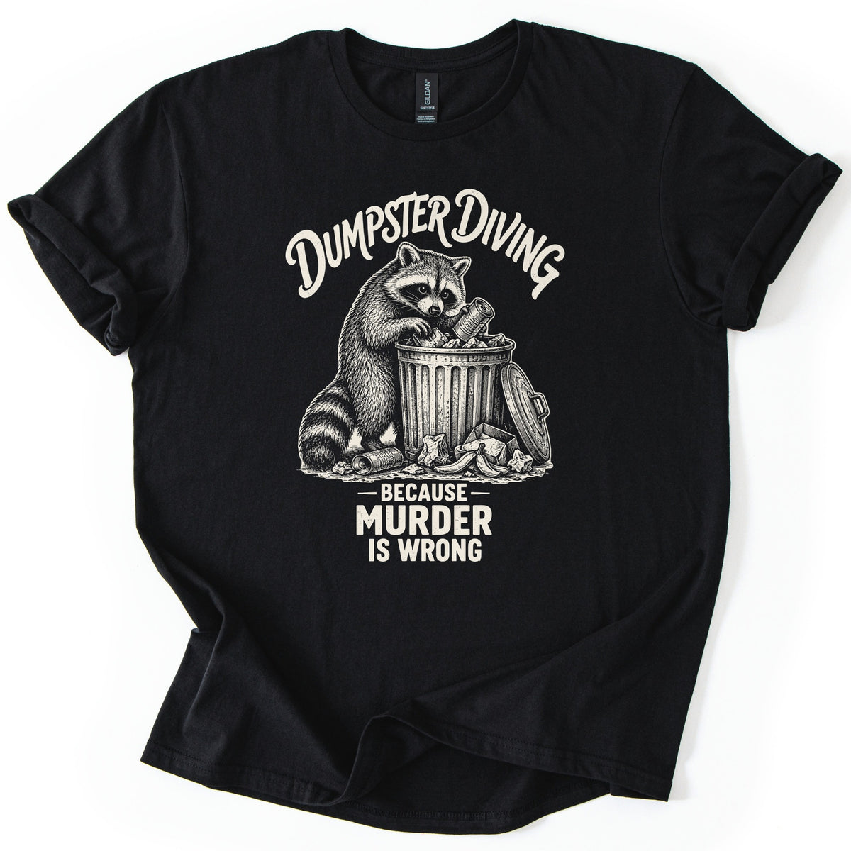 Dumpster Diving Murder Raccoon Comfort Colors T-shirt in Black, laid flat. Cream etching of a raccoon digging through an overflowing trash can under arched script reading Dumpster Diving, with Because Murder Is Wrong below. Sleeves rolled on a white background.
