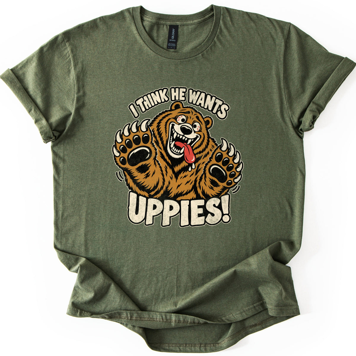 I Think He Wants Uppies Comfort Colors T-shirt in Military Green, laid flat. A cartoon brown bear with a wide toothy grin and its tongue out raises both clawed paws between the words I Think He Wants and Uppies! The sleeves are cuffed on a white background.