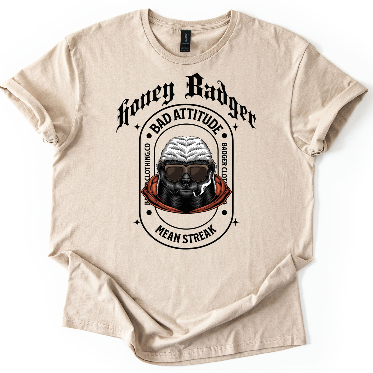 Bad Vibes Badger Comfort Colors T-shirt in Sand, laid flat. Black print: Honey Badger in gothic letters over an oval badge reading Bad Attitude, Badger Clothing.co and Mean Streak around a honey badger in sunglasses and an orange hood, smoking a cigarette. On a white background.
