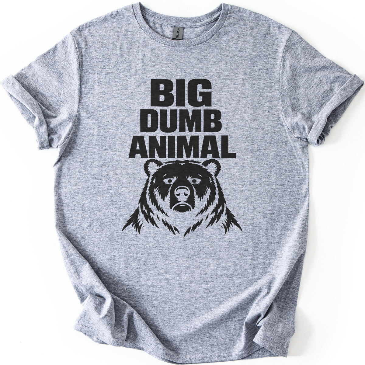 Big Dumb Animal Comfort Colors T-shirt in Sport Grey, laid flat. Bold black letters read BIG DUMB ANIMAL above a black illustration of a stern, front-facing bear head with shaggy fur. The sleeves are rolled and the shirt lies on a white background.