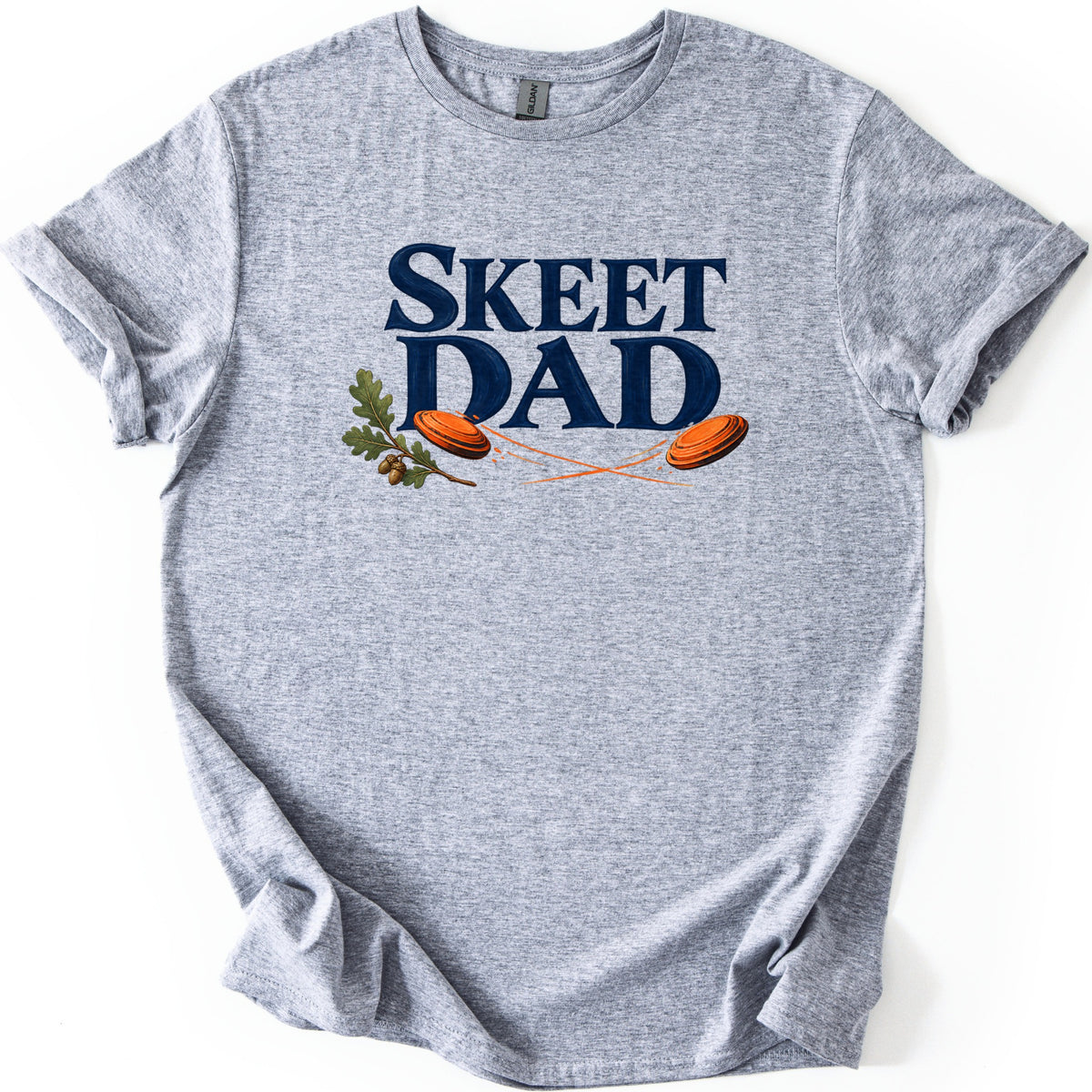 Skeet Dad Comfort Colors T-shirt in Sport Grey, laid flat. The words SKEET DAD in large navy letters, with an oak sprig and acorns on the left and two orange clay targets flying with crossing orange trails. Sleeves are cuffed, on a white background.