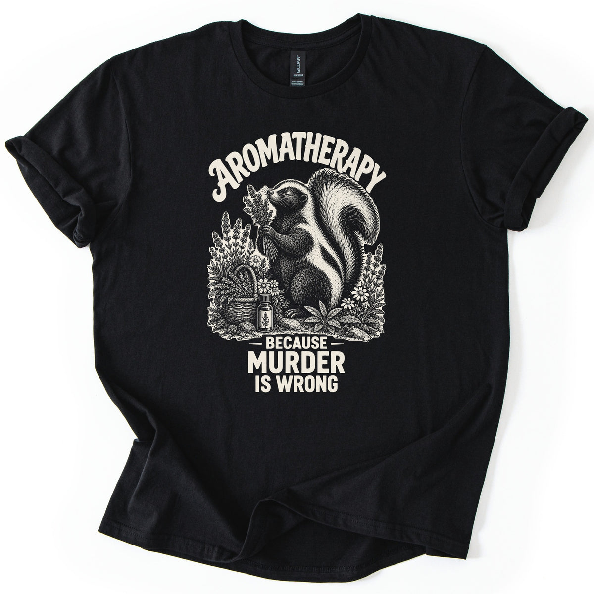 Aromatherapy Murder Skunk Comfort Colors T-shirt in Black, laid flat. A cream skunk sniffs a lavender bundle beside a basket, flowers and an oil bottle, under the word Aromatherapy and above Because Murder Is Wrong. Sleeves are cuffed on a white background.