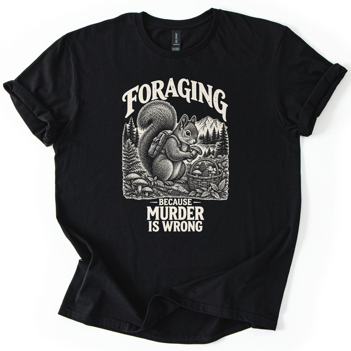 Foraging Murder Squirrel Comfort Colors T-shirt in Black, laid flat. Foraging arches over a cream etched squirrel wearing a backpack and holding a mushroom beside a basket of mushrooms, with pines and a mountain behind. Below: Because Murder Is Wrong. Cuffed sleeves, white background.