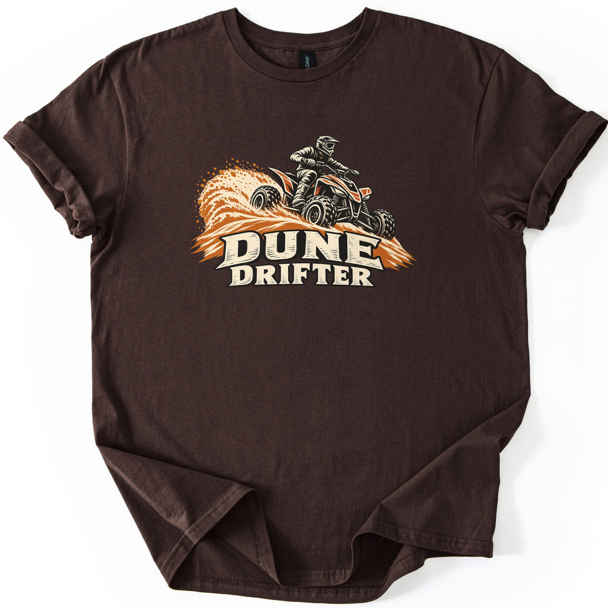 Dune Drifter Comfort Colors T-shirt in Dark Chocolate, laid flat. A helmeted rider on an orange and black four-wheeler throws up a wave of orange sand above the words Dune Drifter in cream letters. The shirt has cuffed sleeves and lies on a white background.