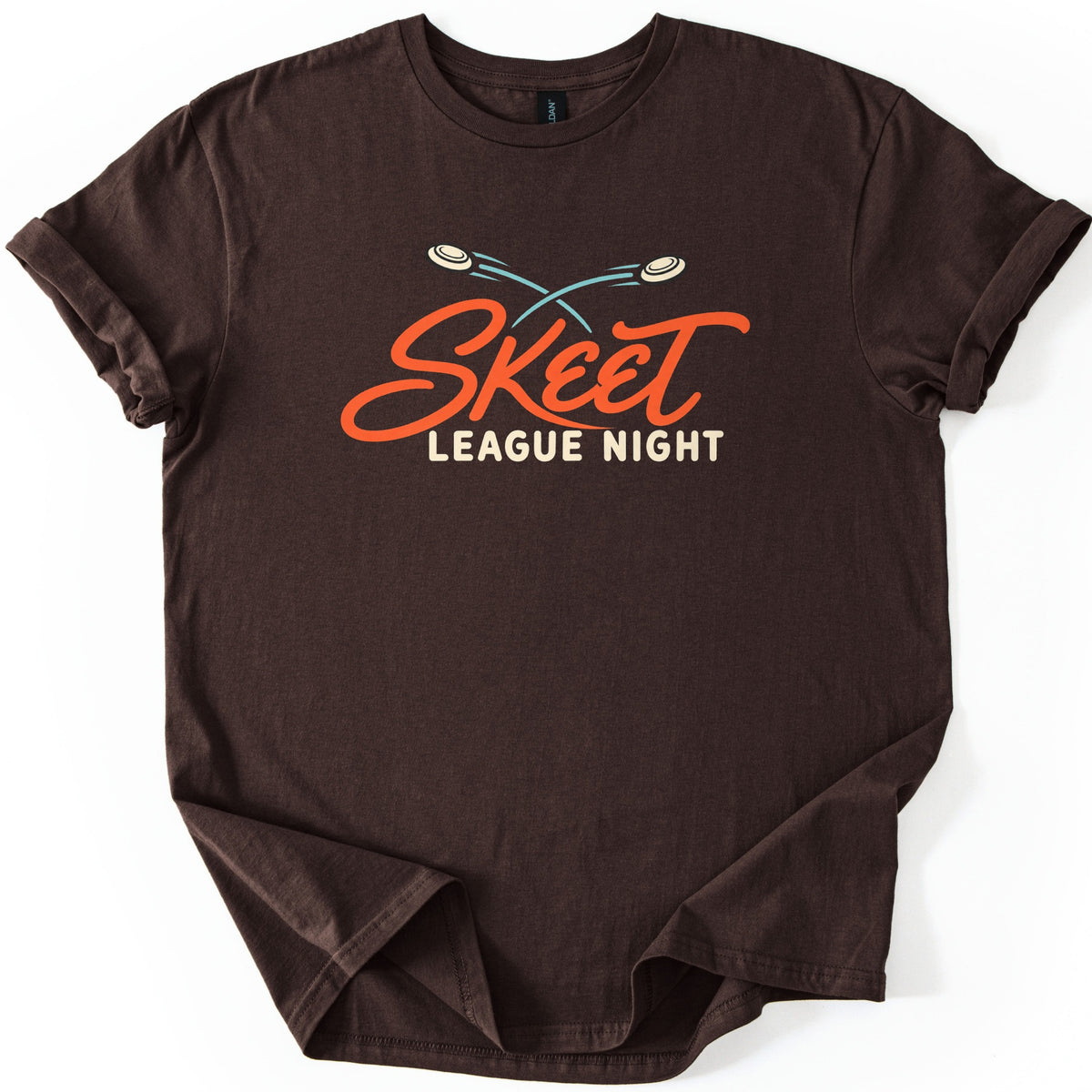 Skeet League Night Comfort Colors T-shirt in Dark Chocolate, laid flat. Two cream clay targets with crossing teal trails fly above the word Skeet in orange script, with League Night in cream capitals below. The shirt has rolled sleeves on a white background.