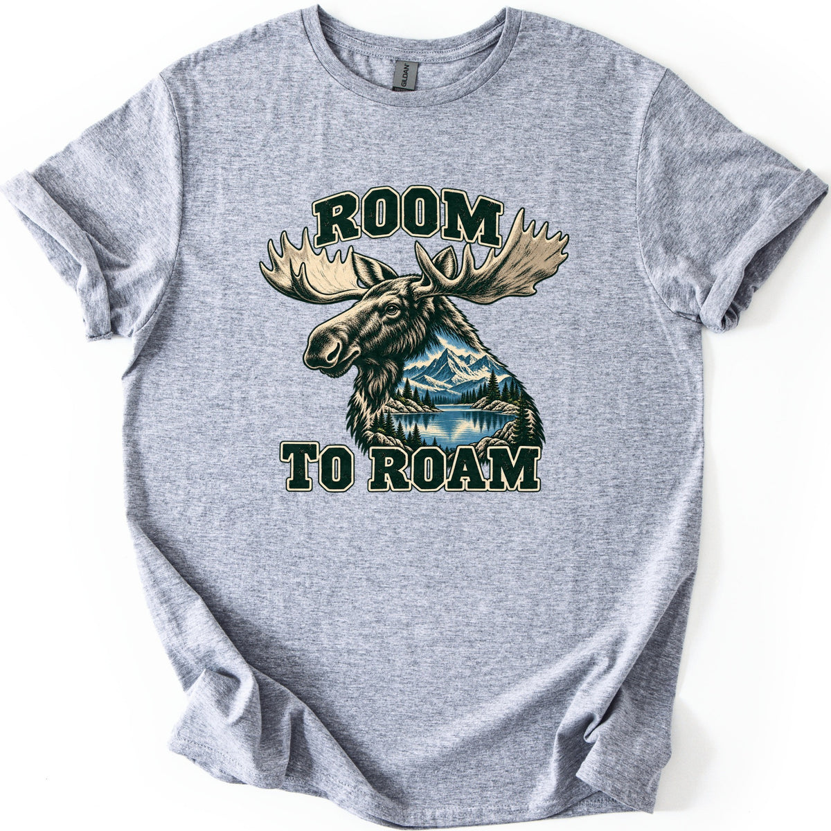 Room to Roam Comfort Colors T-shirt in Sport Grey, laid flat. A moose head with large pale antlers, its neck filled with a scene of snowy mountains, pine trees and a blue lake, between the words ROOM and TO ROAM in dark green block letters. Sleeves rolled, on a white background.