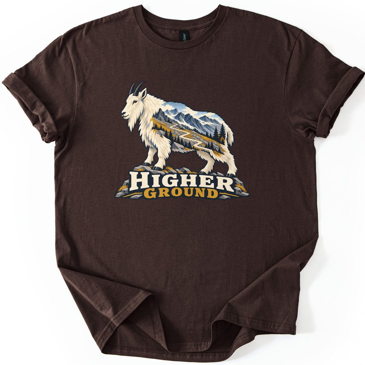 Higher Ground Comfort Colors T-shirt in Dark Chocolate, laid flat. A white mountain goat on gray rocks shows a landscape of snowy mountains, pines, golden grass and a winding trail inside its body, above the words Higher Ground. The sleeves are cuffed on a white background.