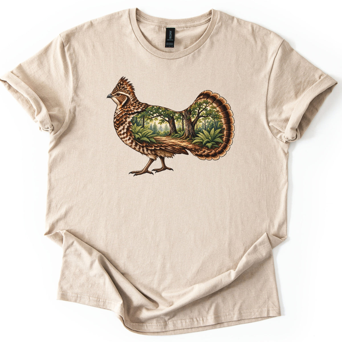 Ruffed Grouse Woods Comfort Colors T-shirt in Sand, laid flat. A walking ruffed grouse with a crested head and barred brown feathers, its body and fanned tail filled with a forest scene of trees, ferns and a dirt path. No words. Sleeves rolled, on a white background.