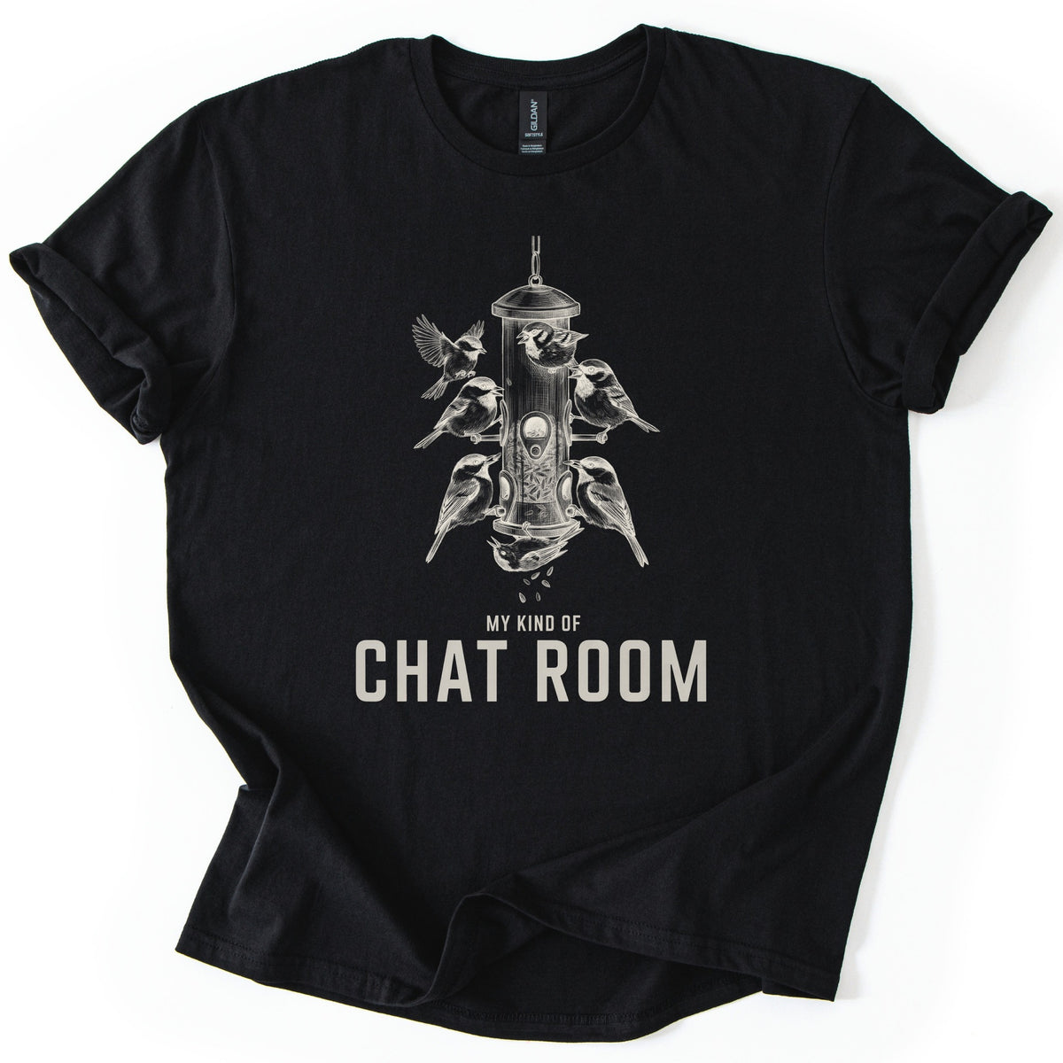 My Kind Of Chat Room Comfort Colors T-shirt in Black, laid flat. A cream sketch of chickadees and sparrows perched around a hanging tube bird feeder, one upside down below spilling seeds, above the words My Kind Of Chat Room. Sleeves rolled, on a white background.