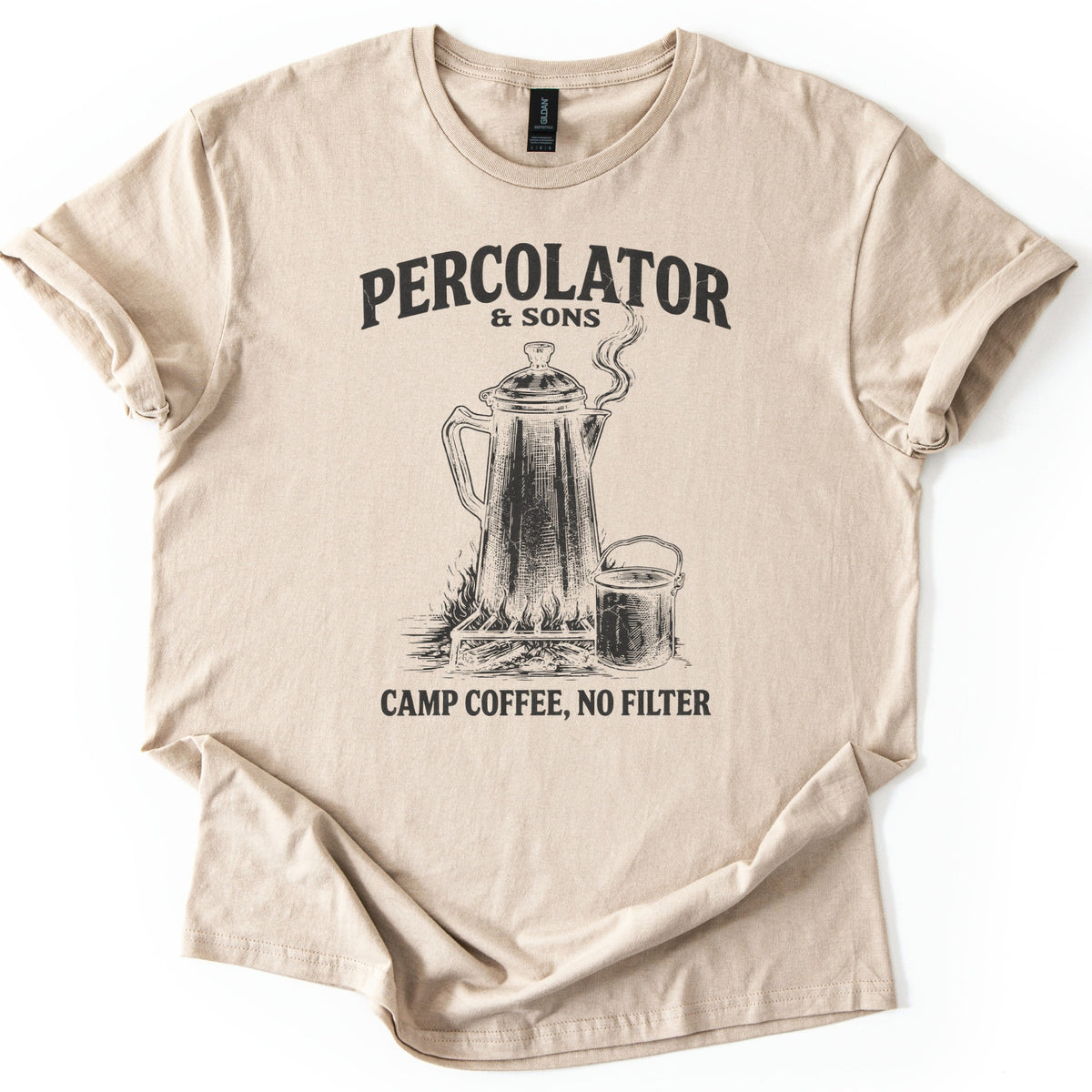 Percolator & Sons Comfort Colors T-shirt in Sand, laid flat. A sketched coffee percolator steams on a grate over a campfire beside a tin cup, under the words Percolator & Sons and above Camp Coffee, No Filter, in black ink. The sleeves are rolled on a white background.