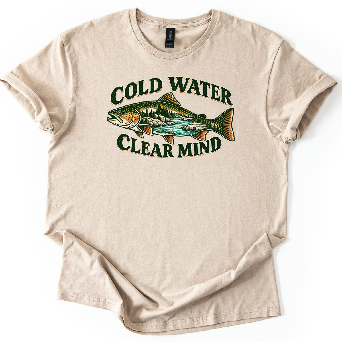 Cold Water Clear Mind Comfort Colors T-shirt in Sand, laid flat. A speckled trout whose body holds a scene of pine trees, rocks and a turquoise river sits between the words Cold Water and Clear Mind in dark green. The sleeves are cuffed on a plain white background.