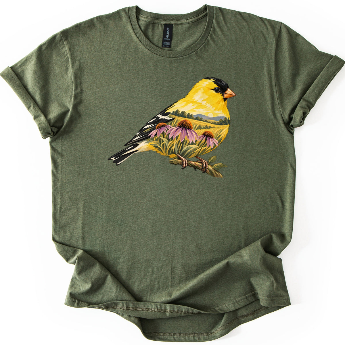 Goldfinch Meadow Comfort Colors T-shirt in Military Green, laid flat. A goldfinch in yellow, black and white perches on a branch; inside its body is a meadow scene with coneflowers, tall grass, trees and hills under a pale sky. No words. Cuffed sleeves, white background.