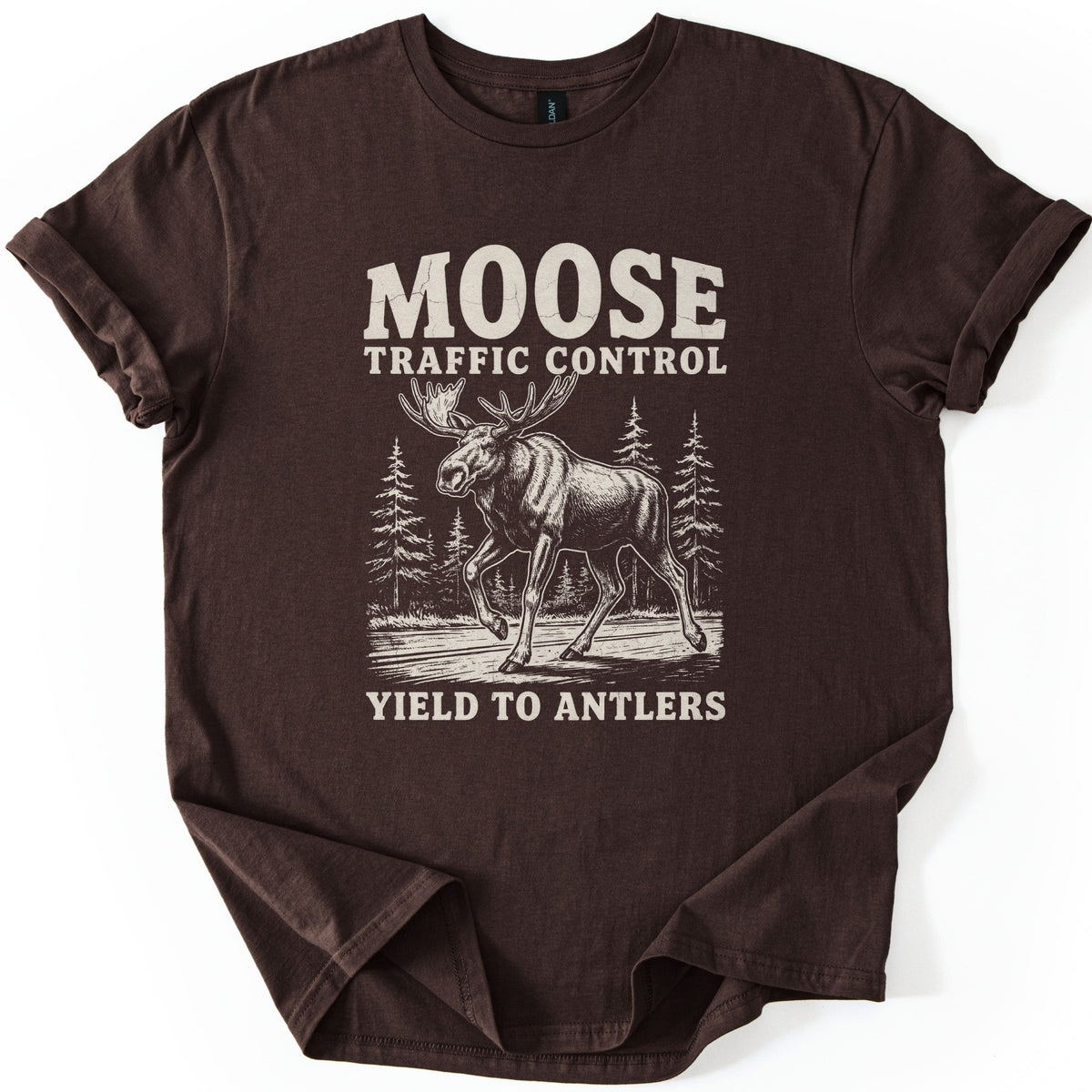 Moose Traffic Control Comfort Colors T-shirt in Dark Chocolate, laid flat. A cream engraved-style moose striding across a road with pine trees behind it, below the words Moose Traffic Control and above Yield to Antlers. The sleeves are cuffed, on a white background.