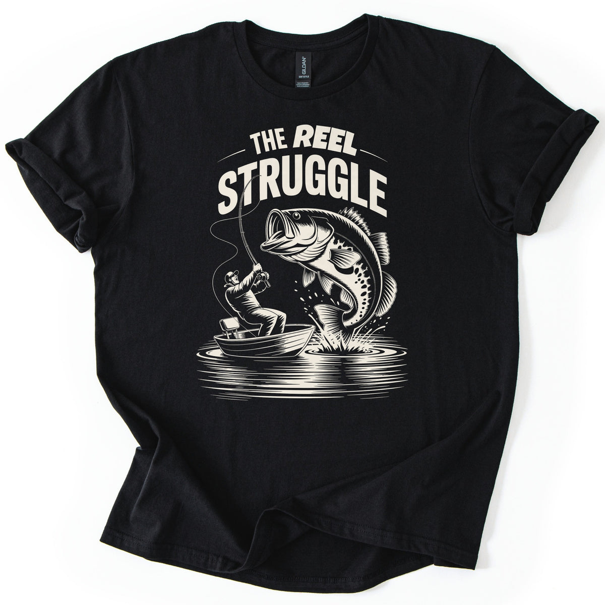 Reel Struggle Comfort Colors T-shirt in Black, laid flat. Cream print of the words The Reel Struggle above a fisherman in a small boat leaning back on a bent rod as a large bass leaps open-mouthed from the water. The sleeves are rolled, on a white background.