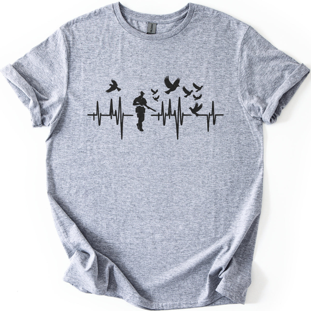 Bird Hunter Comfort Colors T-shirt in Sport Grey, laid flat. A black heartbeat line crosses the chest around a silhouetted hunter in a cap holding a shotgun, with birds flying above and one perched on the line. No words. Cuffed sleeves on a white background.