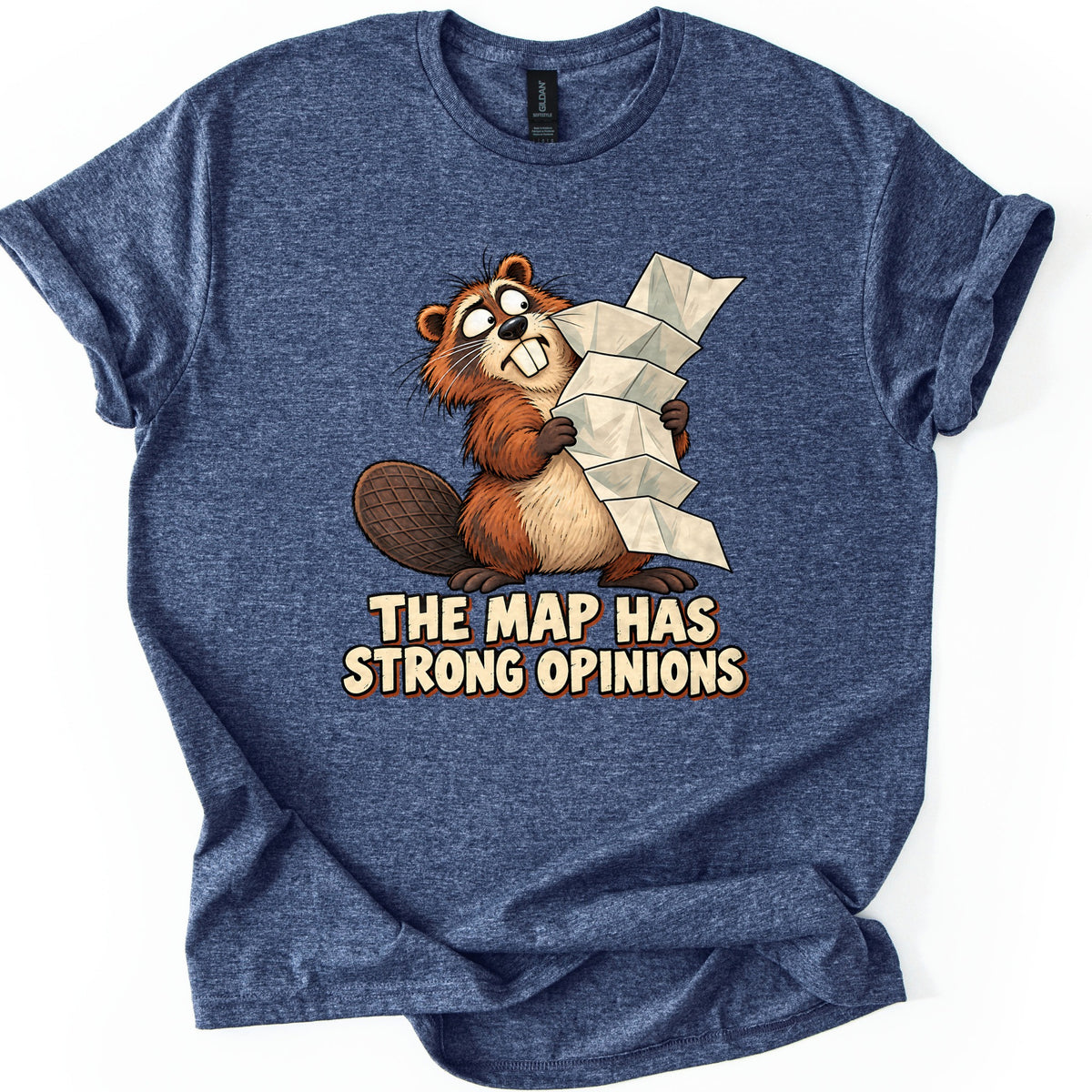 The Map Has Strong Opinions Comfort Colors T-shirt in Heather Navy, laid flat. A cartoon beaver with wide, rolling eyes holds a long, accordion-folded paper map above the words The Map Has Strong Opinions in cream lettering. The heathered shirt lies on a white background with rolled sleeves.