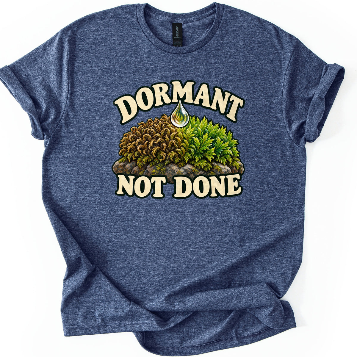 Dormant Not Done Comfort Colors T-shirt in Heather Navy, laid flat. A painted clump of moss on a stone, brown and curled on one side and green on the other, sits under a water drop between cream words Dormant and Not Done. Laid on white with rolled sleeves.