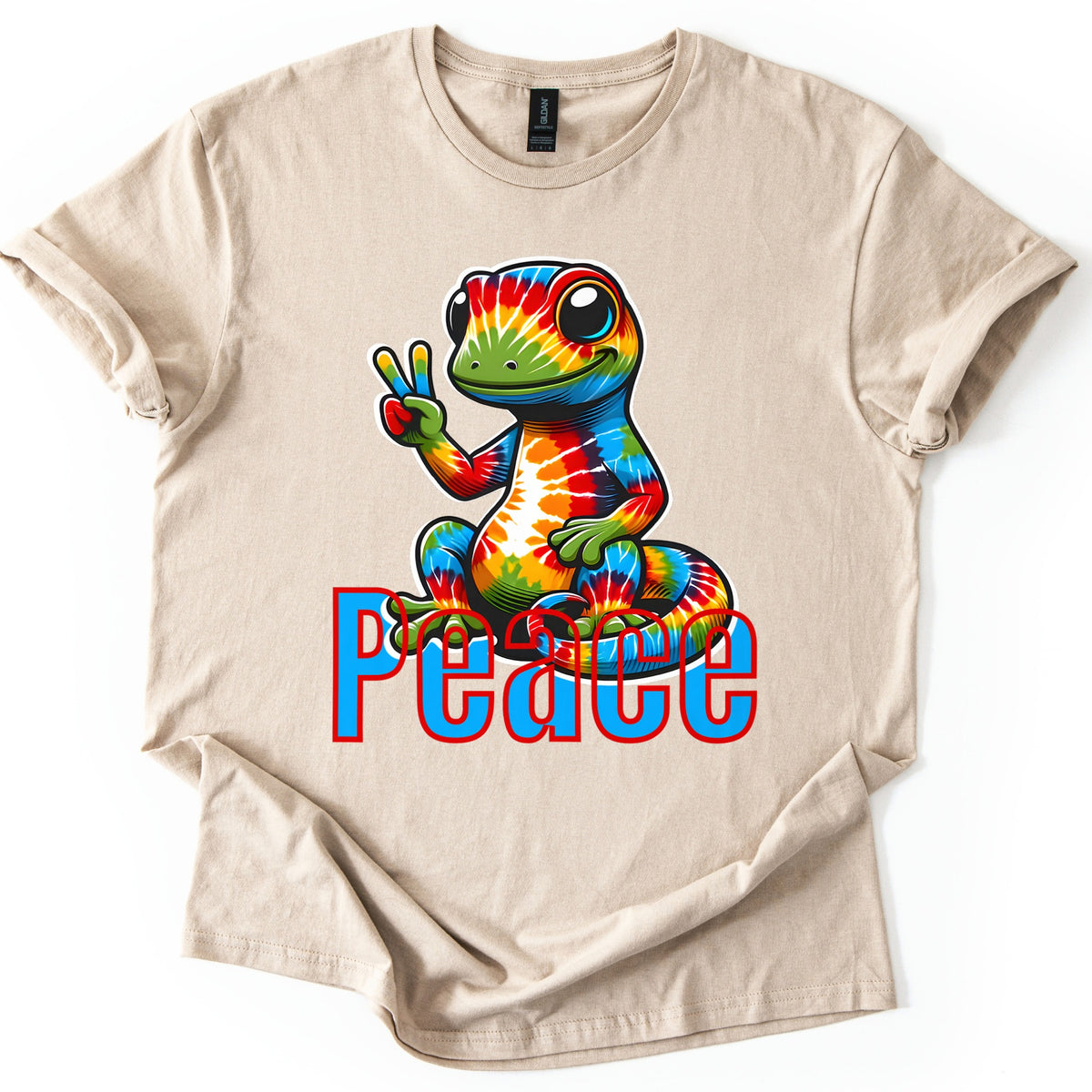 Rainbow Lizard Peace Comfort Colors T-shirt in Sand, laid flat. A smiling cartoon lizard with tie-dye rainbow skin sits on its curled tail and flashes a peace sign above the word Peace in blue letters outlined in red. Cuffed sleeves on a white background.