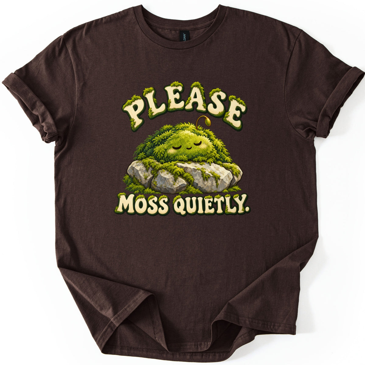 Please Moss Quietly Comfort Colors T-shirt in Dark Chocolate, laid flat. A sleepy, smiling mound of green moss with a tiny sprout rests on gray rocks between the words Please Moss Quietly. in cream letters edged with moss. The sleeves are rolled on a white background.