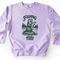 Fishing Because Murder Is Wrong Comfort Colors crewneck sweatshirt in Orchid, laid flat. A dark green sketch-style otter sits on a rock in a lake holding a dripping trout, with pine trees behind it. Fishing arches above it and Because Murder Is Wrong is below. Set on a white surface.