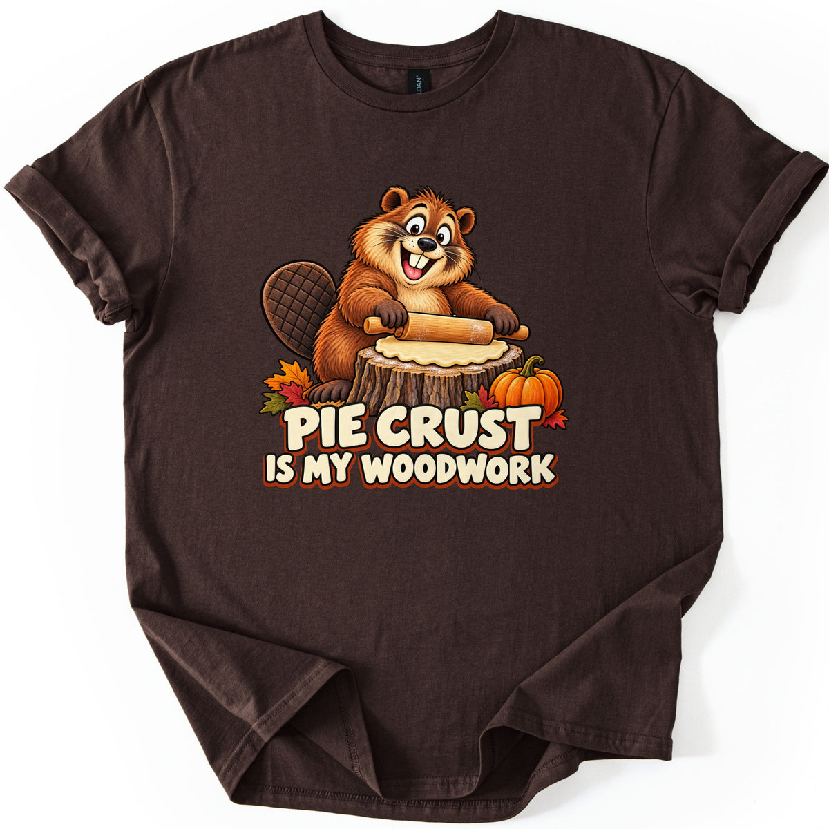 Pie Crust Is My Woodwork Comfort Colors T-shirt in Dark Chocolate, laid flat. A cheerful cartoon beaver uses a rolling pin to flatten pie dough on a tree stump, with a pumpkin and autumn leaves, above the words Pie Crust Is My Woodwork. Cuffed sleeves, on a white background.