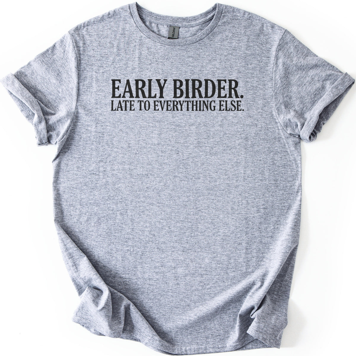 Early Birder Comfort Colors T-shirt in Sport Grey, laid flat. Black serif capital letters across the chest read EARLY BIRDER. LATE TO EVERYTHING ELSE. The shirt lies on a white background with its short sleeves rolled up.