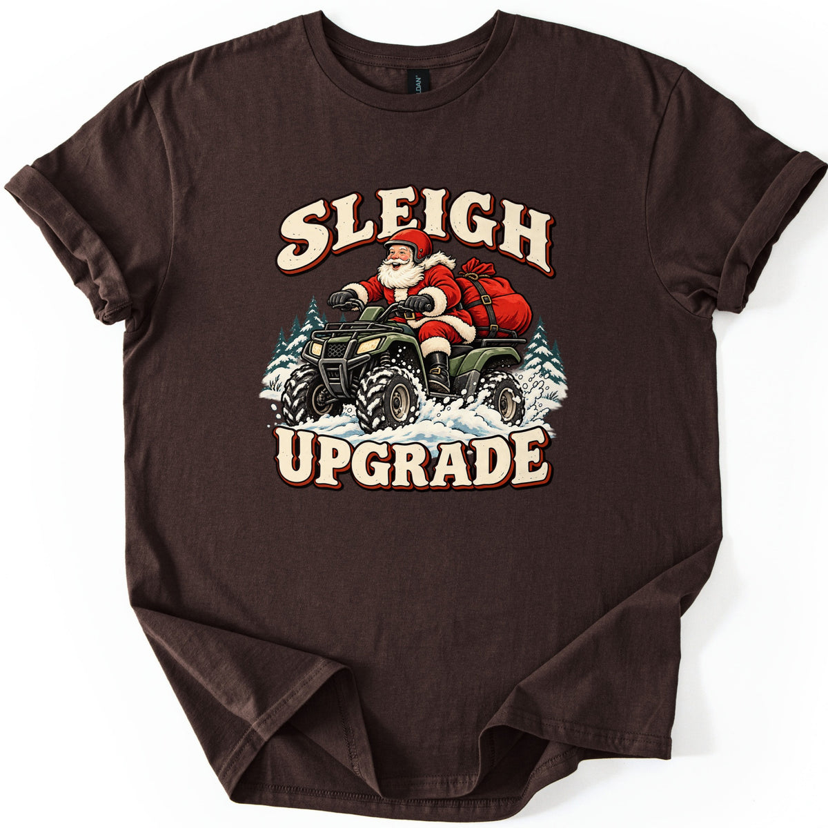 Sleigh Upgrade Comfort Colors T-shirt in Dark Chocolate, laid flat. Smiling Santa in a red helmet rides a green four-wheeler kicking up snow, a red gift sack strapped behind, with the words Sleigh Upgrade. The shirt lies on a white background with rolled sleeves.
