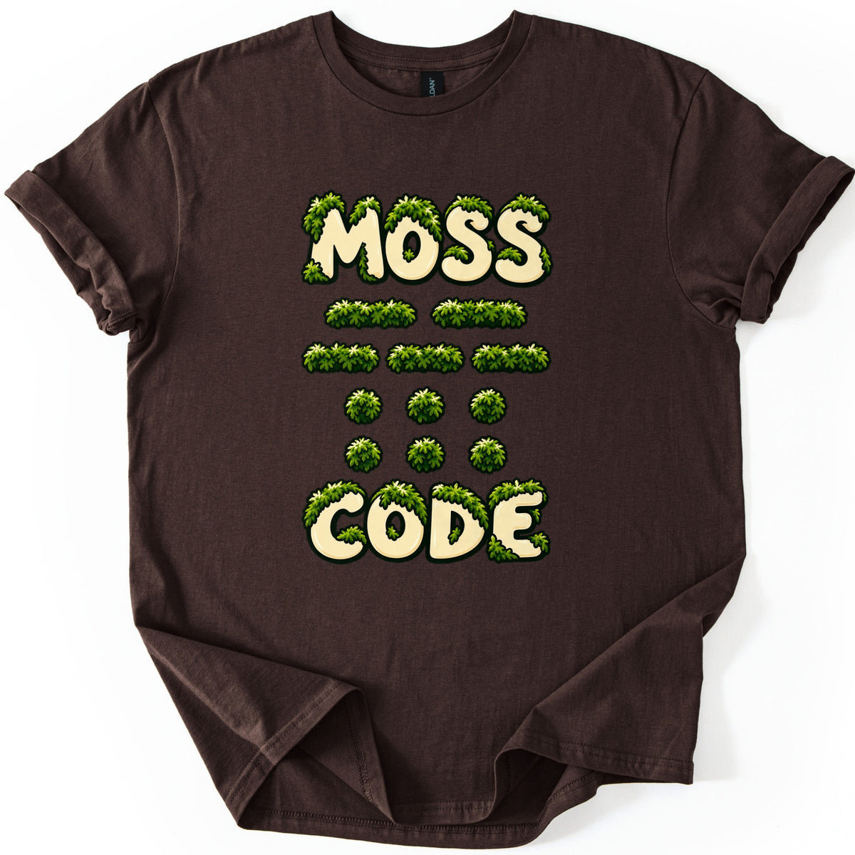 Moss Code Comfort Colors T-shirt in Dark Chocolate, laid flat. Cream bubble letters reading MOSS and CODE are overgrown with green moss, with rows of moss-covered Morse code dashes and dots between them. The shirt has rolled sleeves on a white background.