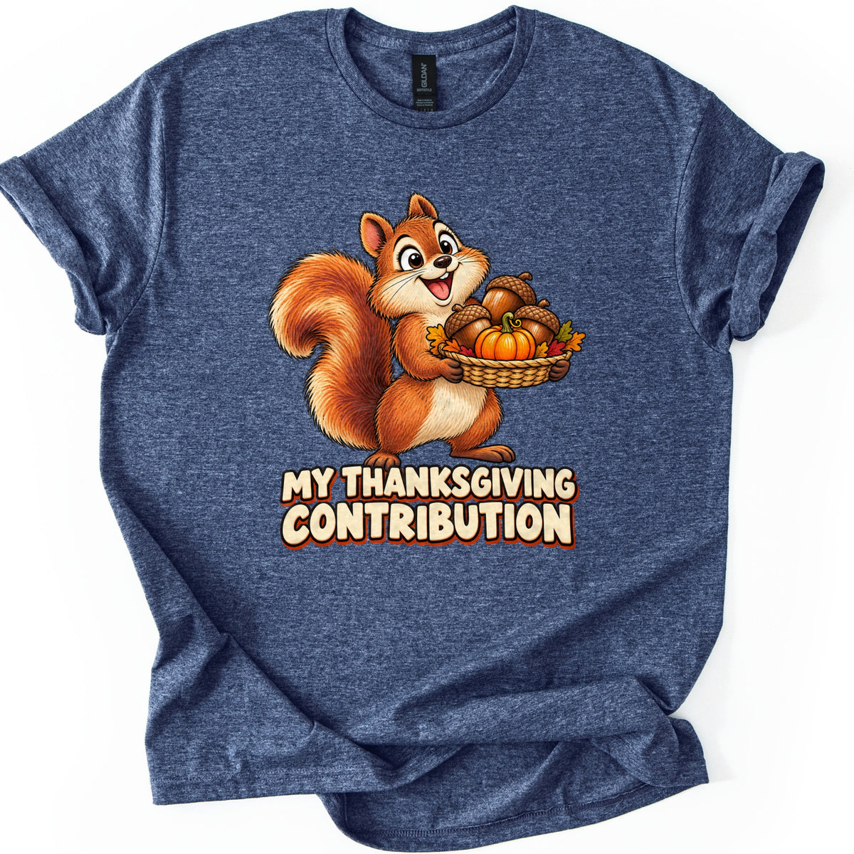 My Thanksgiving Contribution Comfort Colors T-shirt in Heather Navy, laid flat. A happy cartoon squirrel carries a woven basket of acorns, a small pumpkin and autumn leaves above the words My Thanksgiving Contribution in cream letters. The shirt rests on a white background with cuffed sleeves.