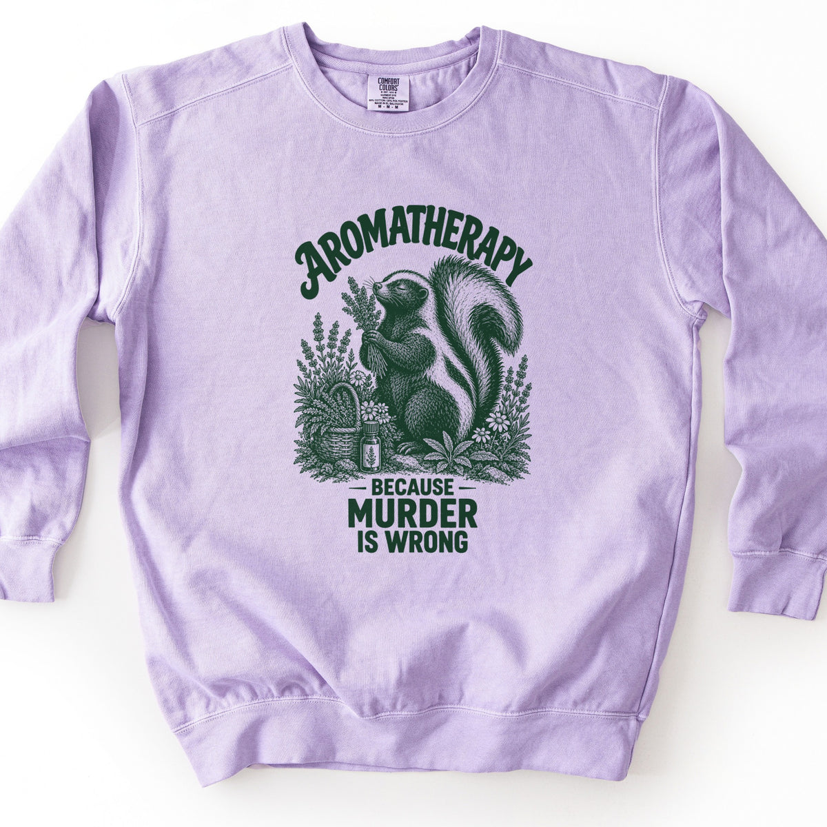 Aromatherapy Because Murder Is Wrong Comfort Colors crewneck sweatshirt in Orchid, laid flat. Dark green line art of a skunk sniffing a bundle of lavender among wildflowers, a basket and an essential oil bottle, with Aromatherapy above and Because Murder Is Wrong below. Shown on a white surface.