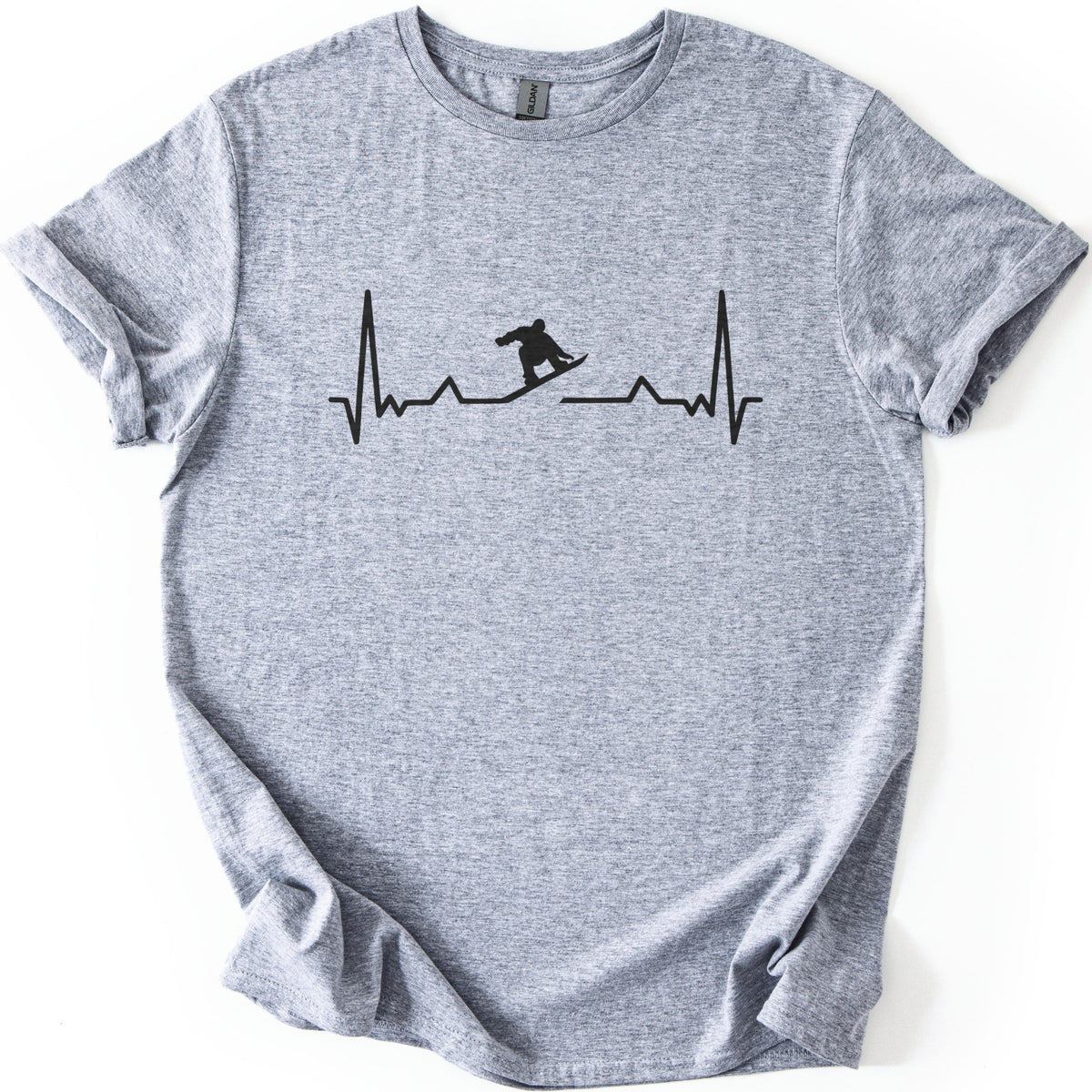 Snow Boarder Pulse II Comfort Colors T-shirt in Sport Grey, laid flat. A black heartbeat line crosses the chest, with a crouching snowboarder silhouette set into a gap in the line; there are no words. The shirt lies on a white surface with its sleeves rolled.