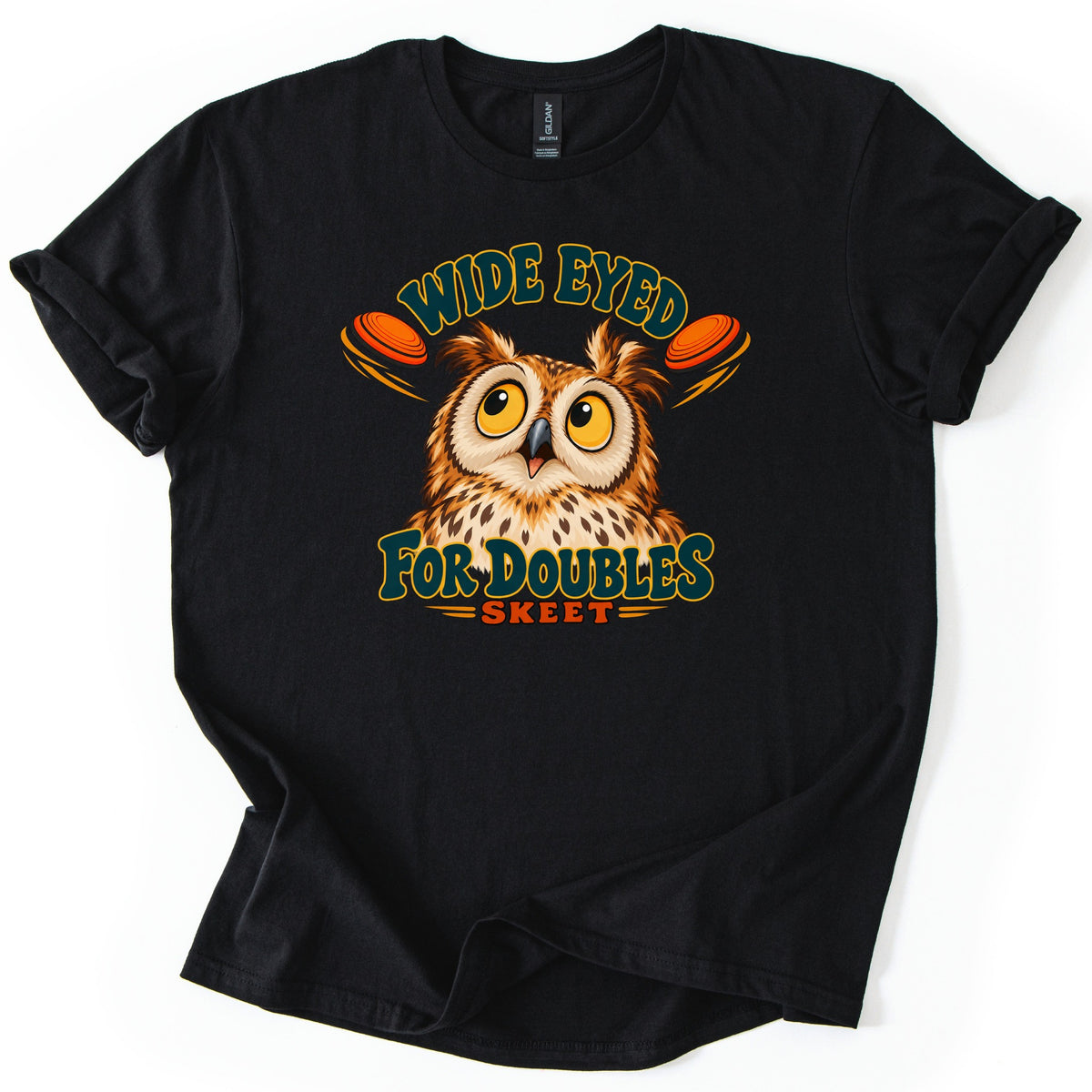 Wide Eyed for Doubles Comfort Colors T-shirt in Black, laid flat. A startled cartoon owl with big yellow eyes sits between two orange clay targets, under the words Wide Eyed and above For Doubles and Skeet. The shirt lies on a white background with cuffed sleeves.