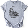 Toad Compost Comfort Colors T-shirt in Sport Grey, laid flat. A black ink etching of a frowning toad in an apron pushing a wheelbarrow of compost, between the words That's it. and You're being returned to the EARTH. Sleeves are cuffed on a white background.