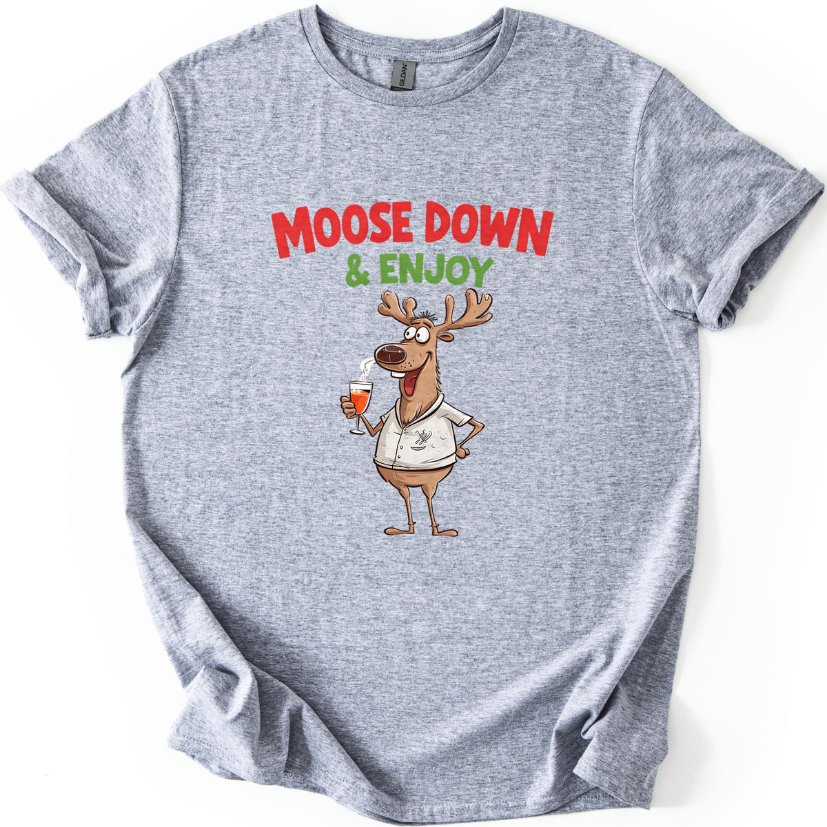 Moose Down And Enjoy Comfort Colors T-shirt in Sport Grey, laid flat. Red words Moose Down above green & Enjoy, over a grinning cartoon moose in a white short-sleeve shirt holding a glass of orange drink, hand on hip. Sleeves are cuffed on a white background.