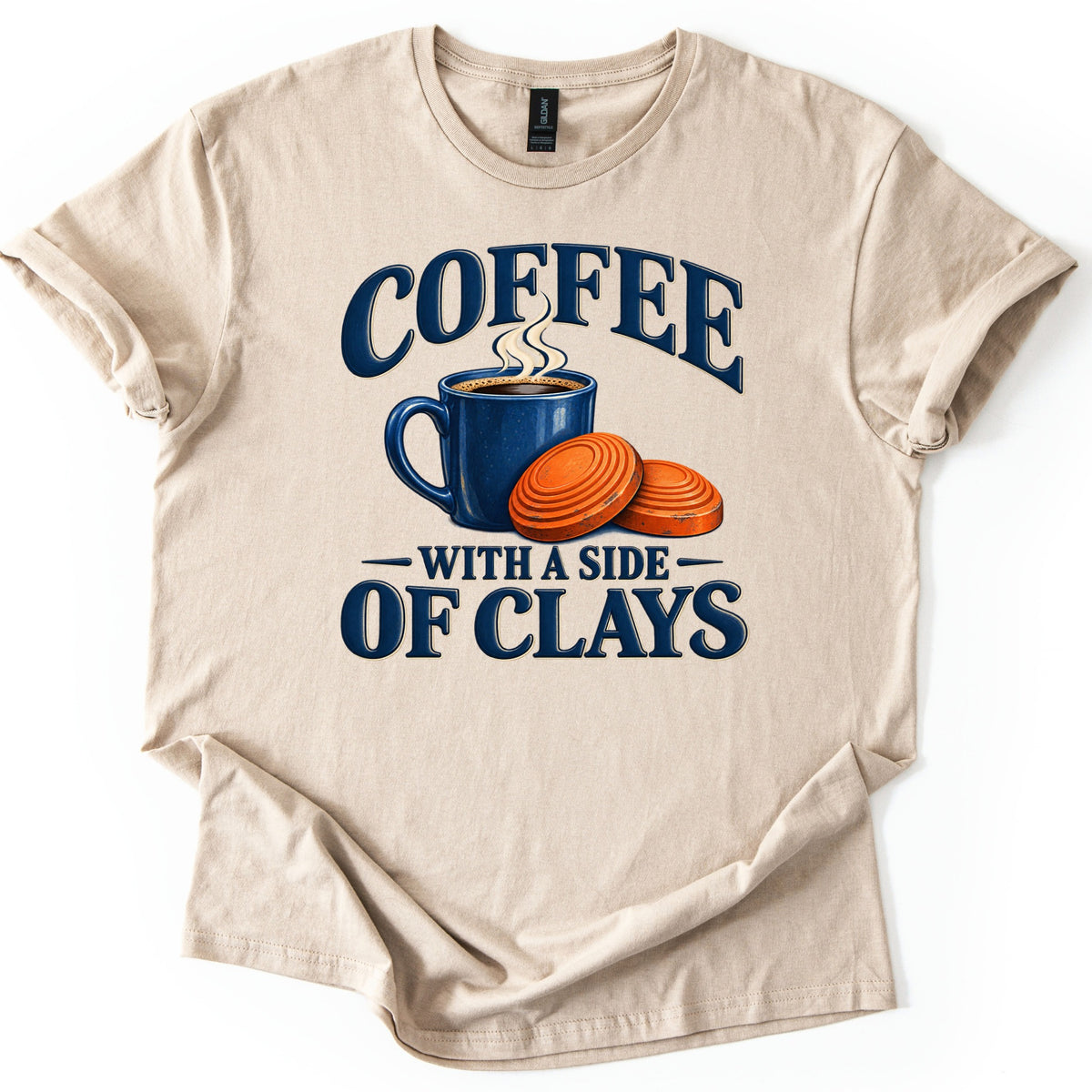 Coffee with a Side of Clays Comfort Colors T-shirt in Sand, laid flat. The print shows a steaming navy coffee mug next to two orange clay targets, framed by the words COFFEE above and WITH A SIDE OF CLAYS below in navy. The shirt rests on a plain white background.