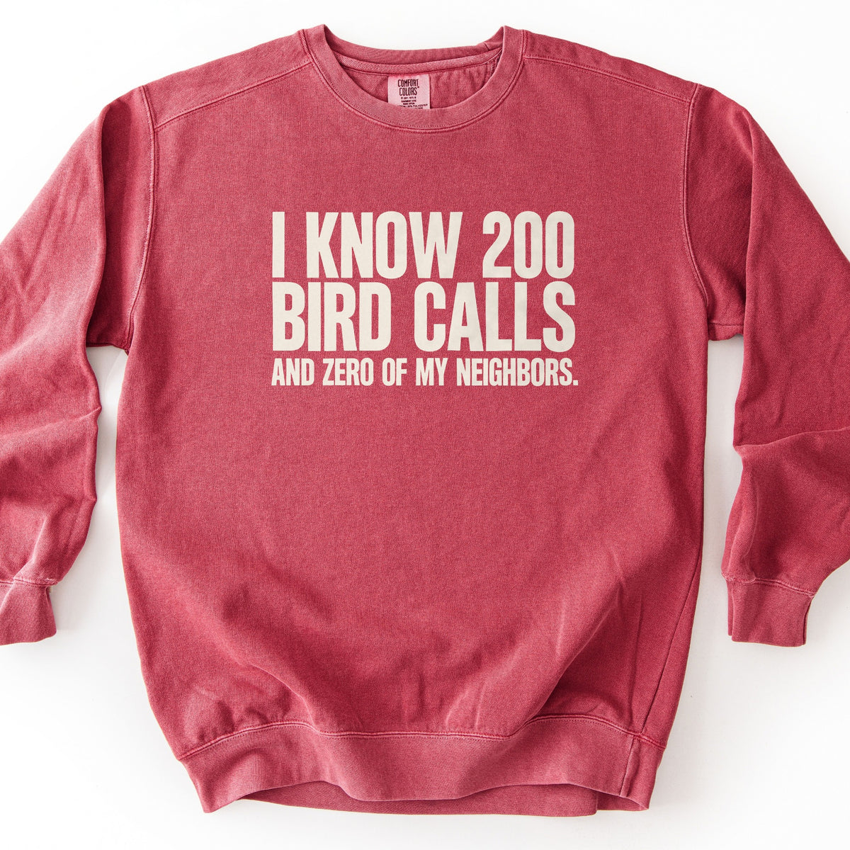 I Know 200 Bird Calls and Zero of My Neighbors Comfort Colors crewneck sweatshirt in Crimson, laid flat. Bold cream capital letters across the chest read I Know 200 Bird Calls, with And Zero of My Neighbors. in smaller letters below. The sweatshirt lies on a plain white background.