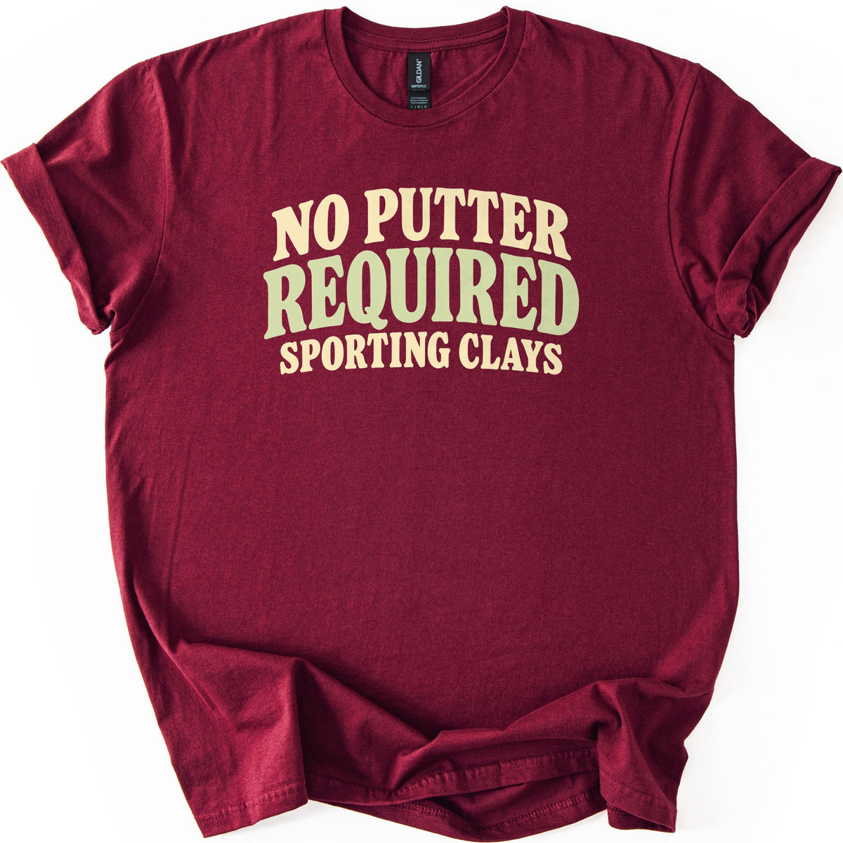 No Putter Required Comfort Colors T-shirt in Maroon, laid flat. Wavy retro letters read NO PUTTER in cream, REQUIRED in larger sage green, and SPORTING CLAYS in cream below. The shirt lies on a white background with rolled sleeves and a gathered hem.