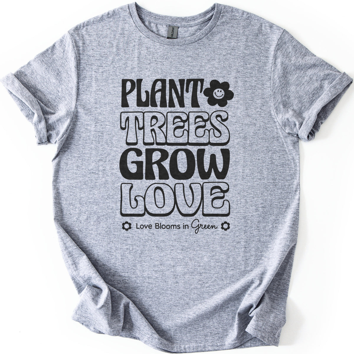 Plant Trees Grow Love Comfort Colors T-shirt in Sport Grey, laid flat. Black retro bubble letters read Plant Trees Grow Love, with a smiling daisy beside Plant and Love Blooms in Green between two small flowers below. Sleeves are rolled on a white background.