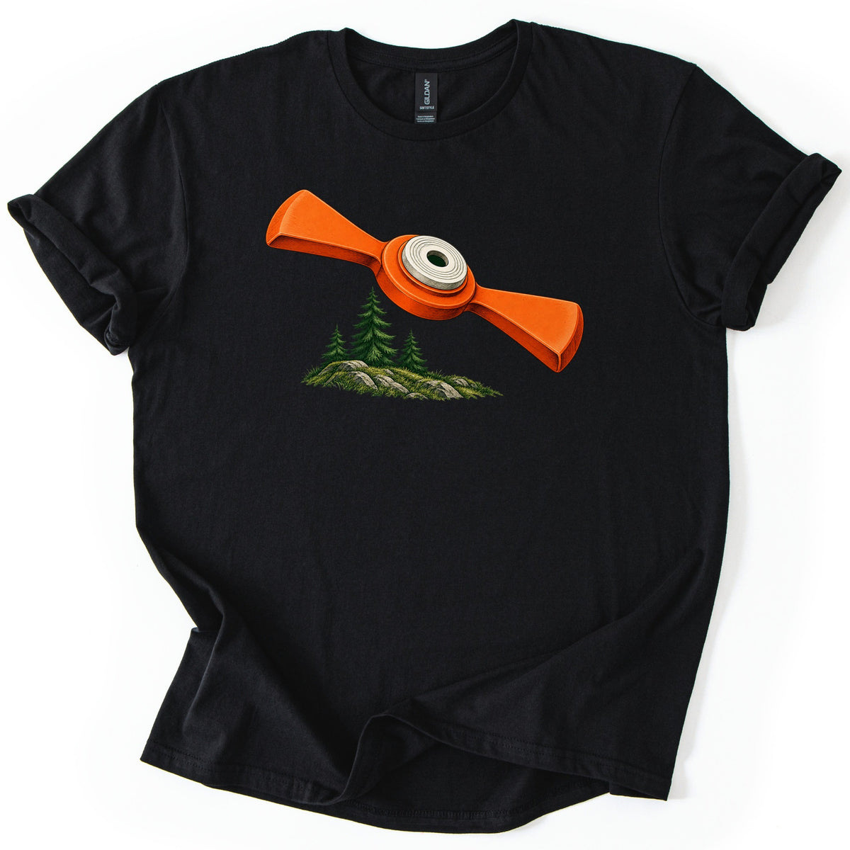 Winged Target Over the Pines Comfort Colors T-shirt in Black, laid flat. A bright orange winged clay target with a white ringed center hovers above three green pine trees on mossy rocks, with no words. The shirt is spread on a white surface, sleeves rolled.