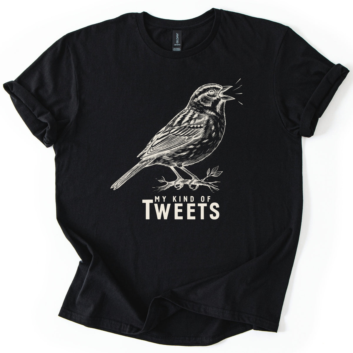 My Kind Of Tweets Comfort Colors T-shirt in Black, laid flat. A cream sketch-style drawing of a sparrow singing on a leafy twig, with short lines by its open beak, above the words My Kind Of Tweets in cream. The sleeves are cuffed and the shirt lies on a white background.