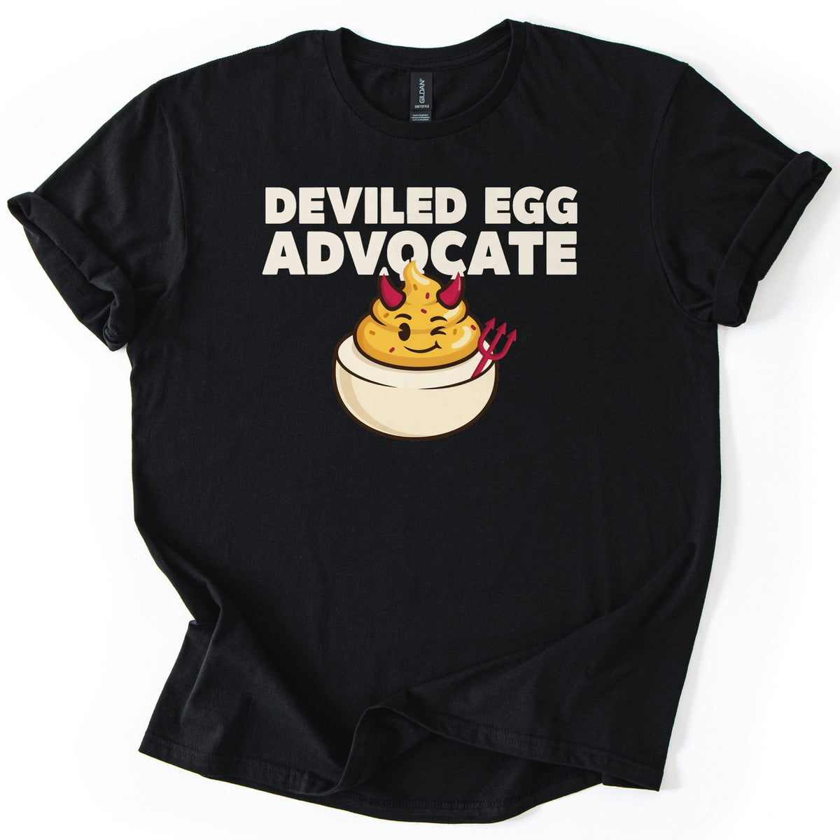 Deviled Egg Advocate Comfort Colors T-shirt in Black, laid flat. Bold cream text reads Deviled Egg Advocate above a cartoon deviled egg with red devil horns, a wink, and a small red pitchfork. The shirt has cuffed sleeves and lies on a white background.