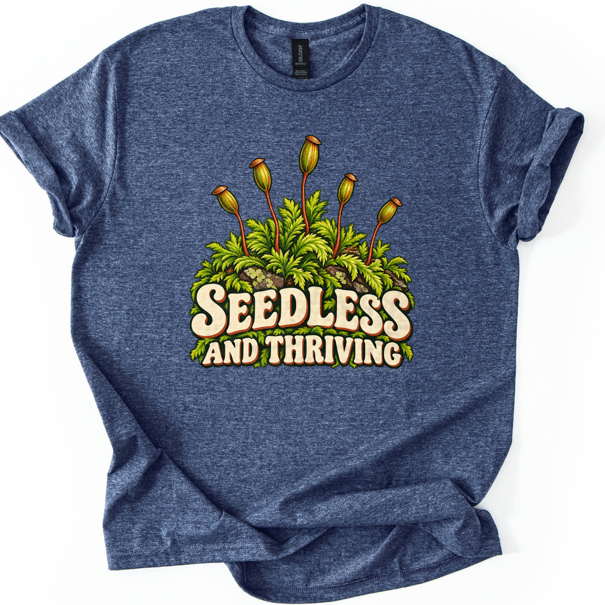 Seedless and Thriving Comfort Colors T-shirt in Heather Navy, laid flat. Green moss with tall reddish stalks topped by spore capsules grows over lichen-dotted rocks above the words SEEDLESS AND THRIVING in cream retro letters. The shirt lies on white with sleeves rolled.