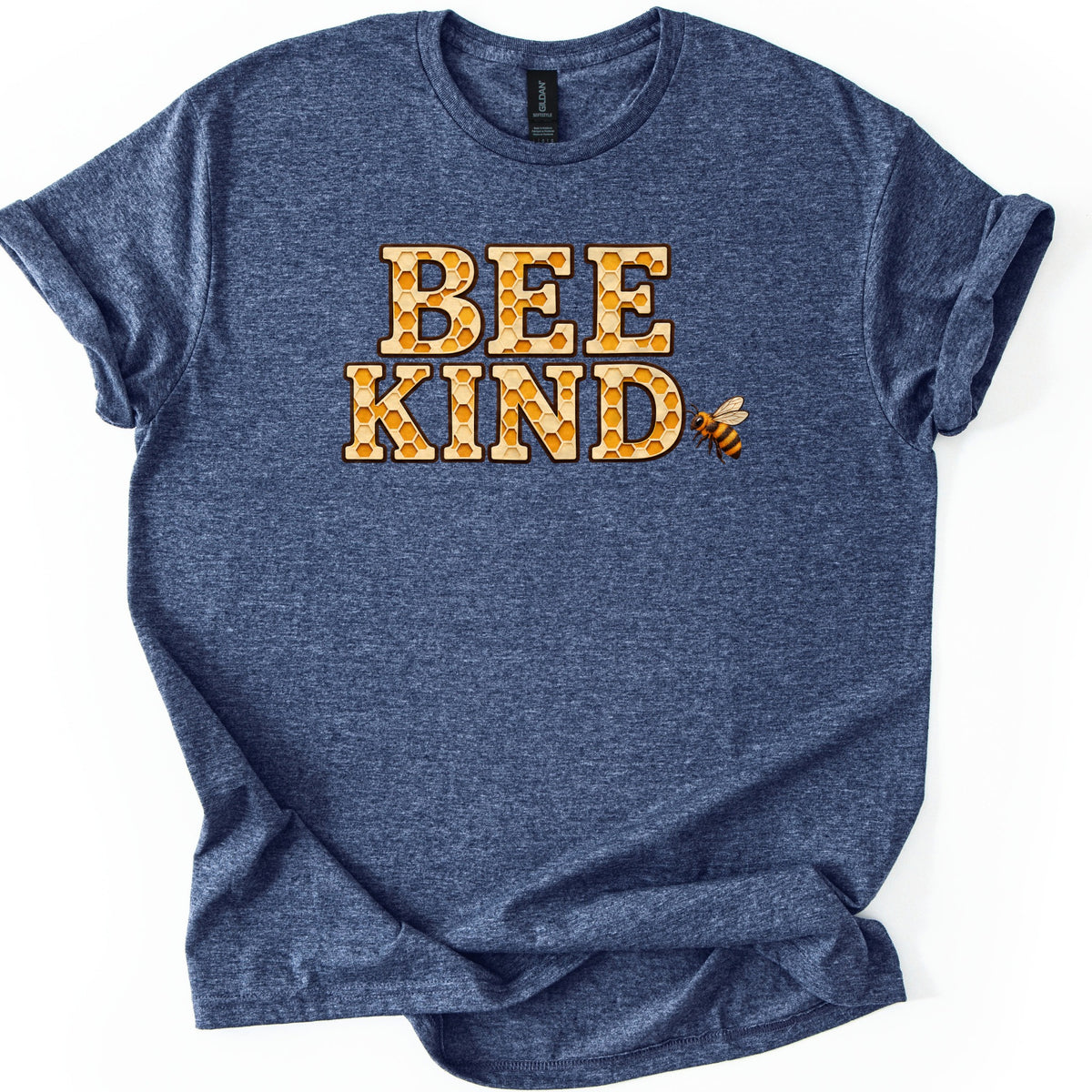 Bee Kind Comfort Colors T-shirt in Heather Navy, laid flat. The words BEE KIND in large block letters filled with a golden honeycomb pattern, with a small honeybee flying next to the D. The shirt has rolled sleeves and lies on a white background.