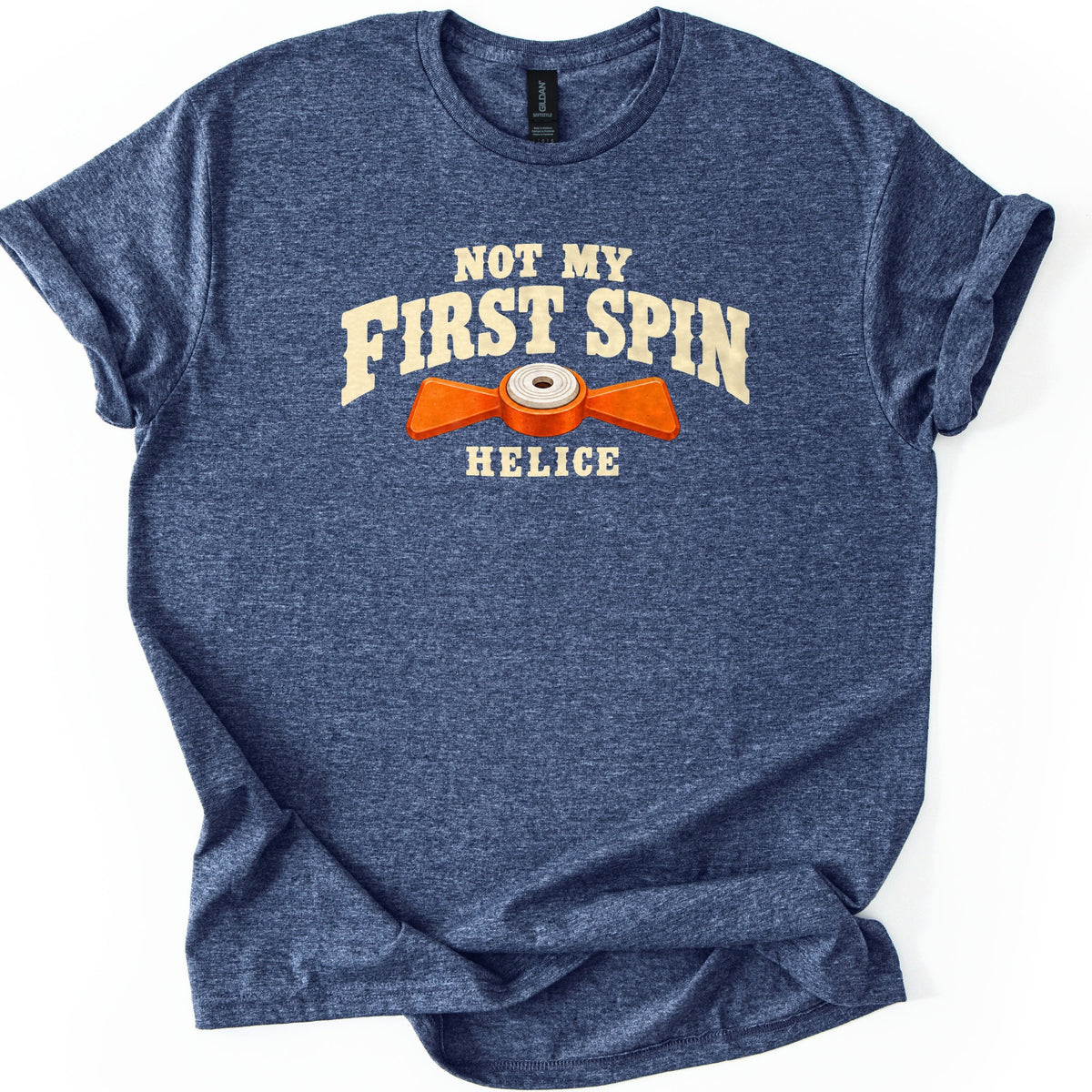 Not My First Spin Comfort Colors T-shirt in Heather Navy, laid flat. Cream western-style letters read Not My First Spin above an orange two-bladed propeller target with a white center, with the word Helice below. The shirt lies on a white surface with sleeves cuffed.
