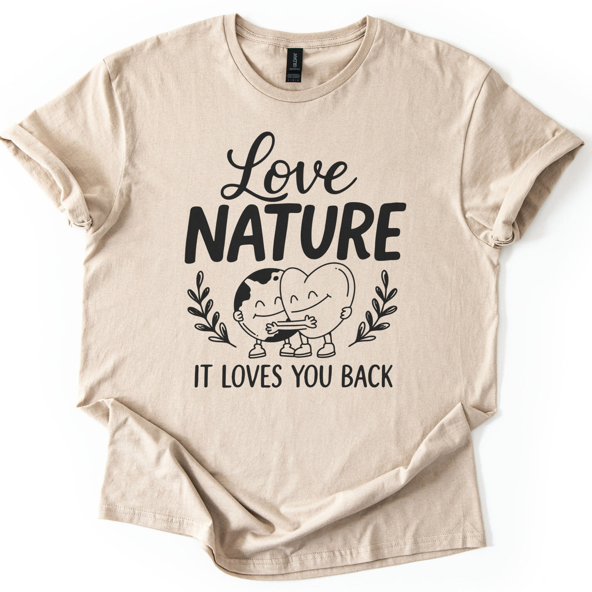 Nature Loves You Back Comfort Colors T-shirt in Sand, laid flat. Black print reads Love NATURE above a smiling cartoon Earth and heart hugging between two leafy sprigs, then IT LOVES YOU BACK. The sleeves are rolled and the shirt lies on a white background.
