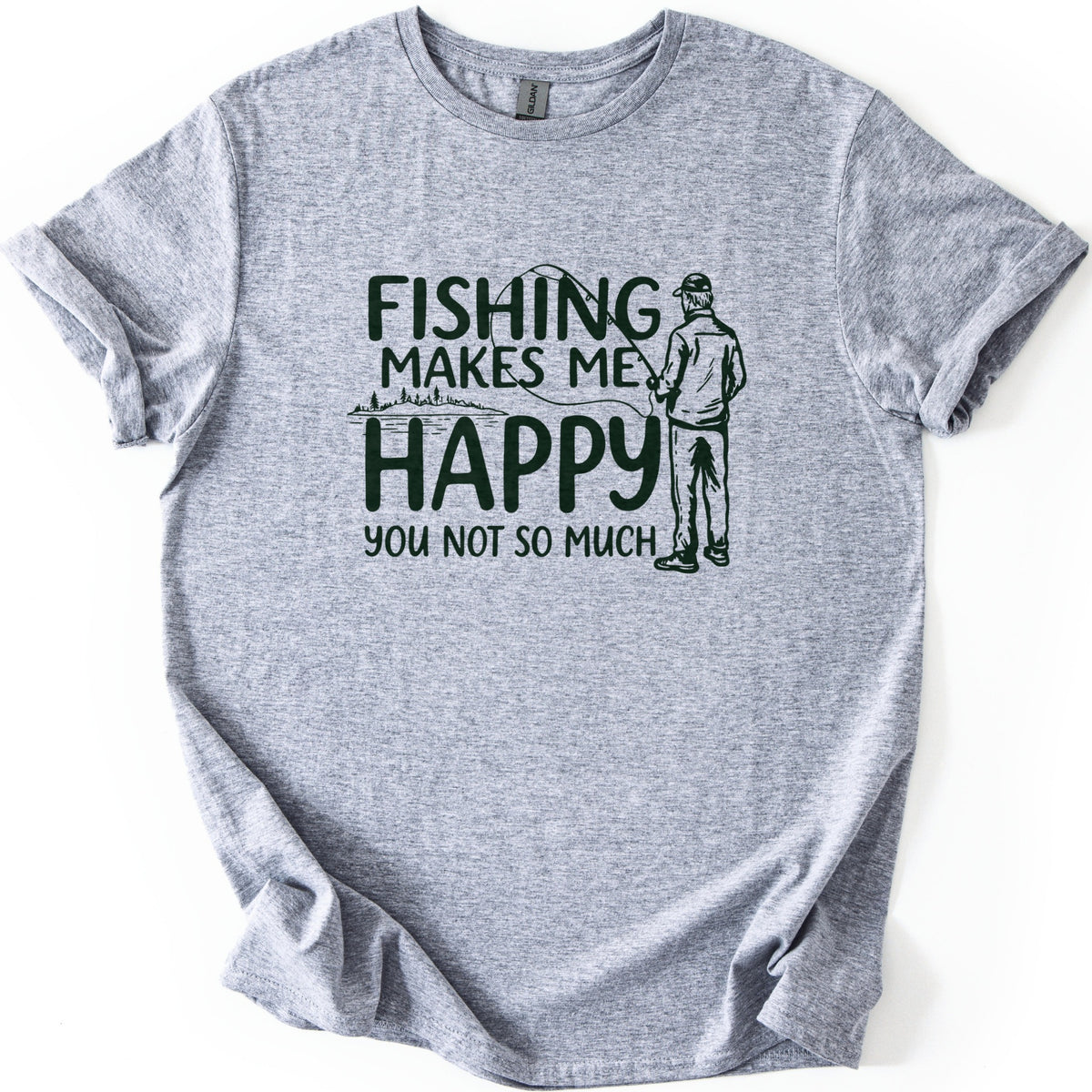Fishing Makes Me Happy Comfort Colors T-shirt in Sport Grey, laid flat. Dark green print reads Fishing Makes Me Happy, You Not So Much, with a line drawing of a capped man fishing, seen from behind, and a lakeshore with trees. Sleeves are rolled on a white background.