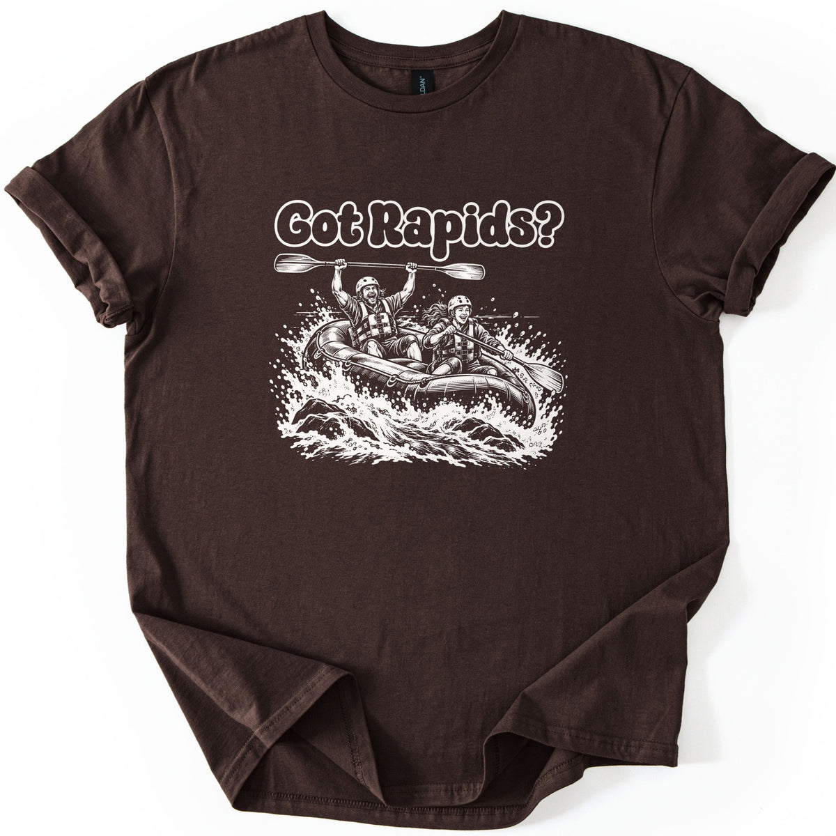 Got Rapids Comfort Colors T-shirt in Dark Chocolate, laid flat. White line art shows a man raising a paddle overhead and a smiling woman paddling a raft through splashing whitewater, under the words Got Rapids? The sleeves are rolled on a white background.