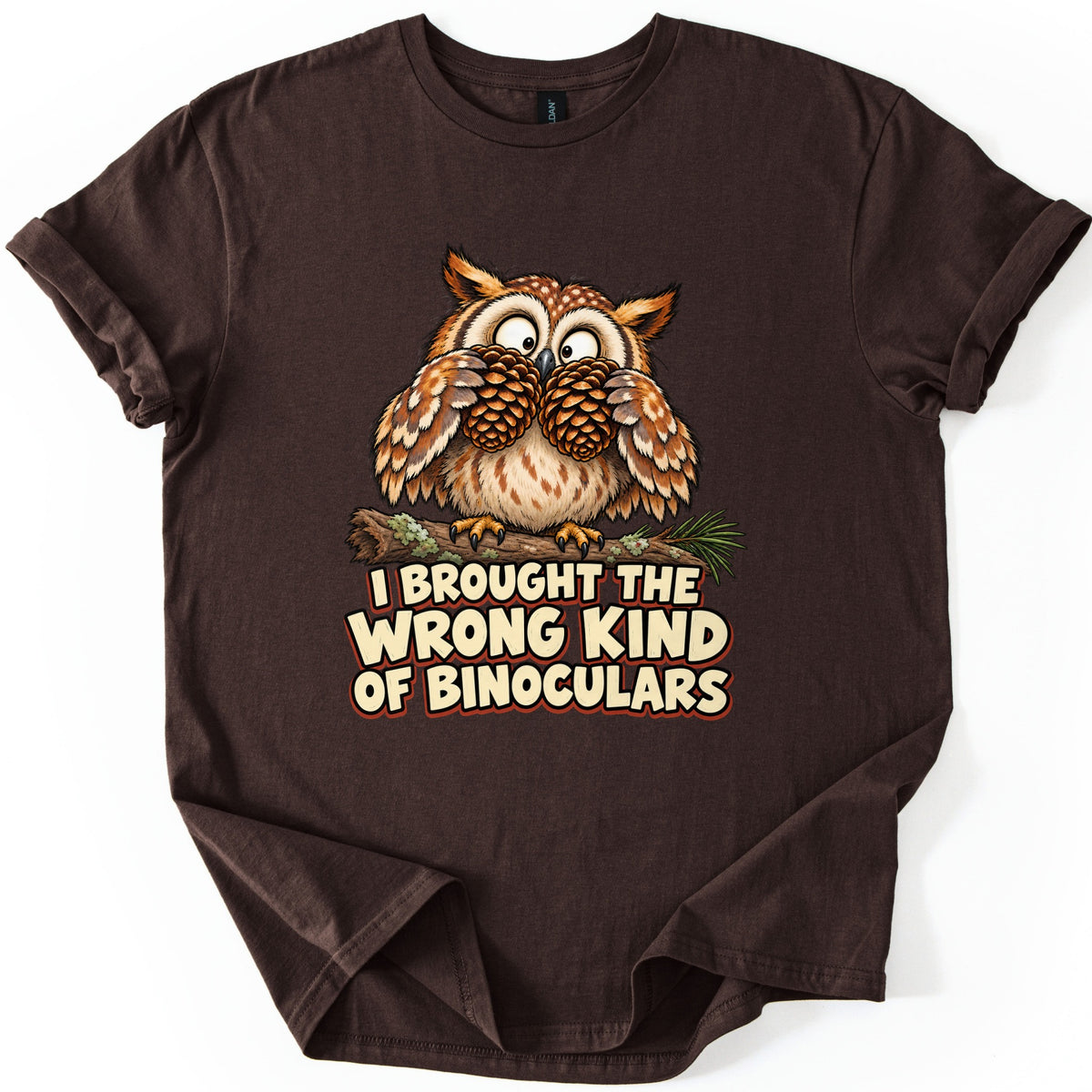 I Brought The Wrong Kind Of Binoculars Comfort Colors T-shirt in Dark Chocolate, laid flat. A wide-eyed cartoon owl on a mossy branch with a pine sprig holds two pine cones to its eyes like binoculars, above the words I Brought The Wrong Kind Of Binoculars in cream letters. Rolled sleeves, white background.