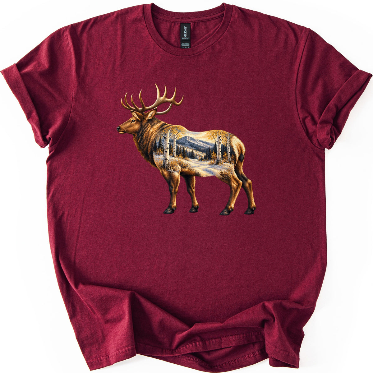 Aspen Pass Elk Comfort Colors T-shirt in Maroon, laid flat. A realistic bull elk stands facing left, its body filled with a snowy mountain trail lined with white aspens in golden leaves and dark pines. No words. The shirt lies on white, bottom bunched.