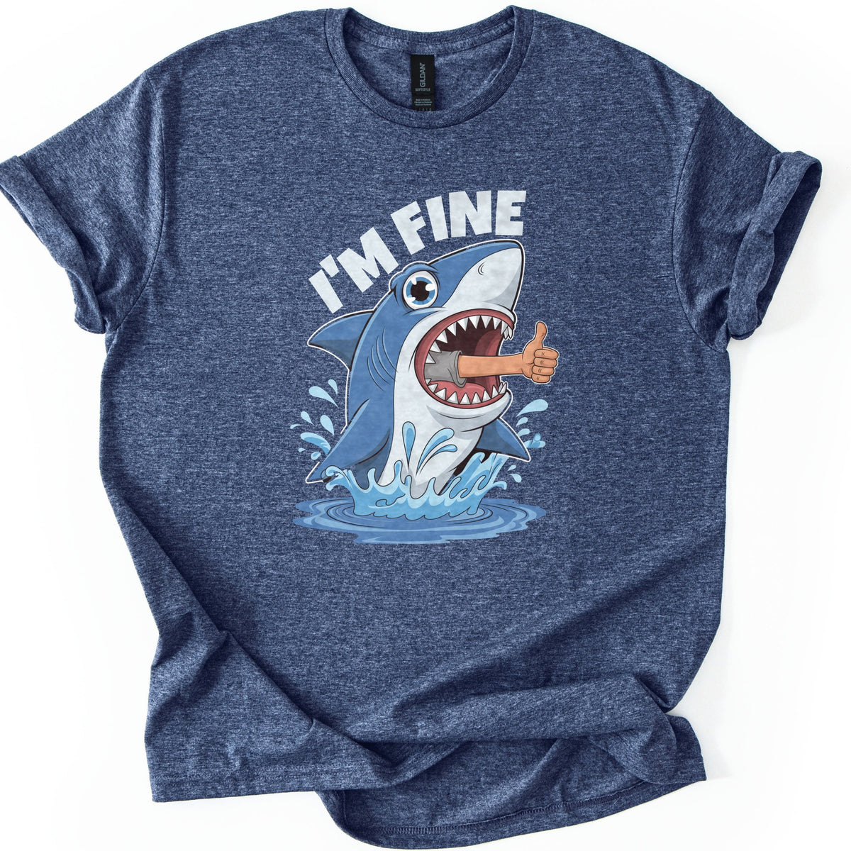 Shark I'm Fine Comfort Colors T-shirt in Heather Navy, laid flat. A cartoon blue shark leaps from splashing water with a human arm giving a thumbs up sticking out of its open mouth, under the words I'M FINE in white. The shirt has rolled sleeves on a white background.